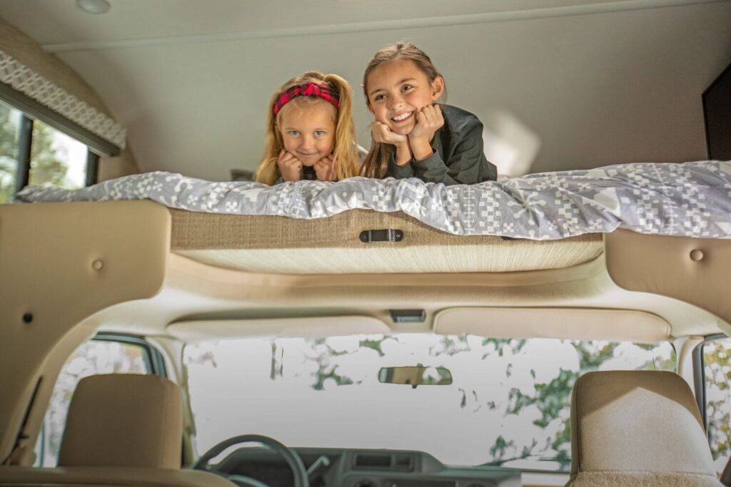 Kids smiling in cabover bunk of Class C RV