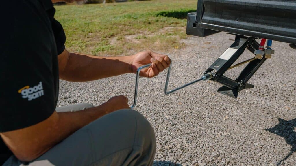 RV technician using crank handle to operate scissor jacks to stabilize RV