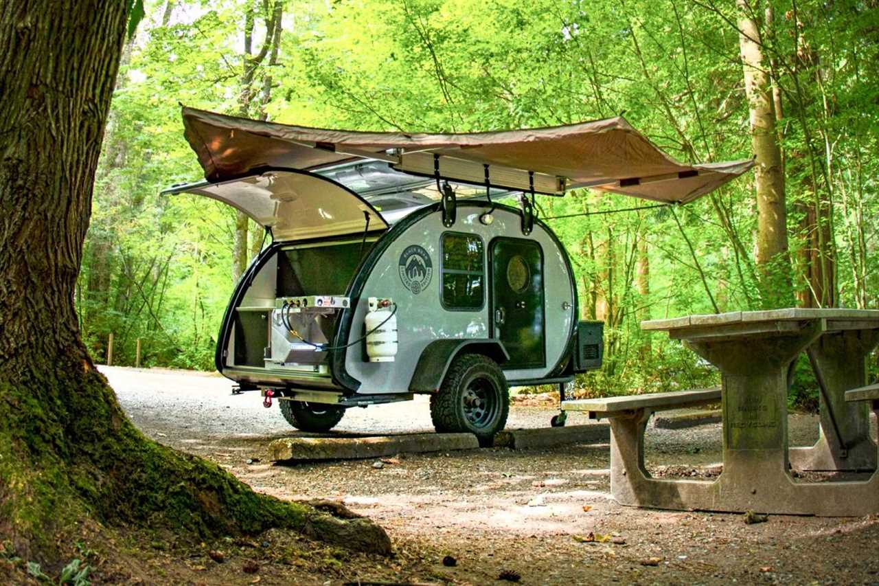 Teardrop travel trailer parked at a campsite in the woods with awning and trunk open