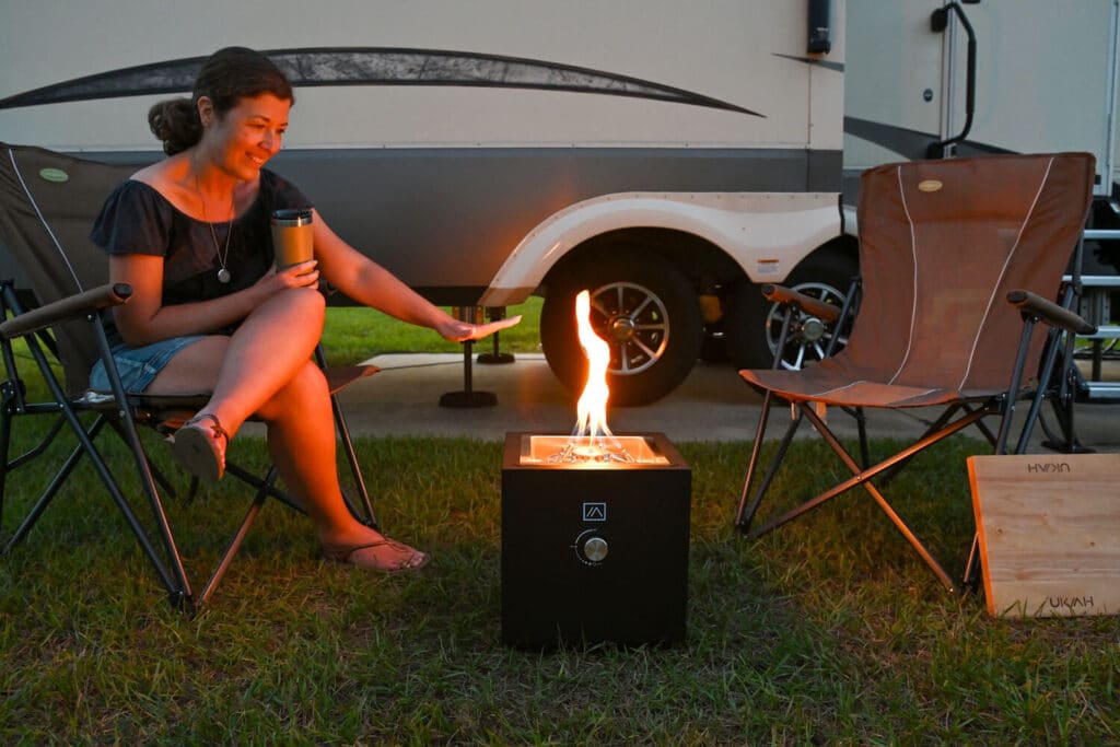 Woman holding hand out to feel heat from portable gas firepit