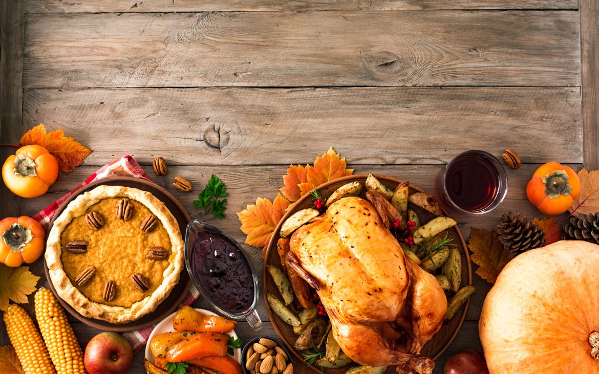 Thanksgiving dinner with chicken, cranberry sauce, pumpkin pie, wine, seasonal vegetables and fruits on wooden table, copy space. Traditional autumn holiday food concept.