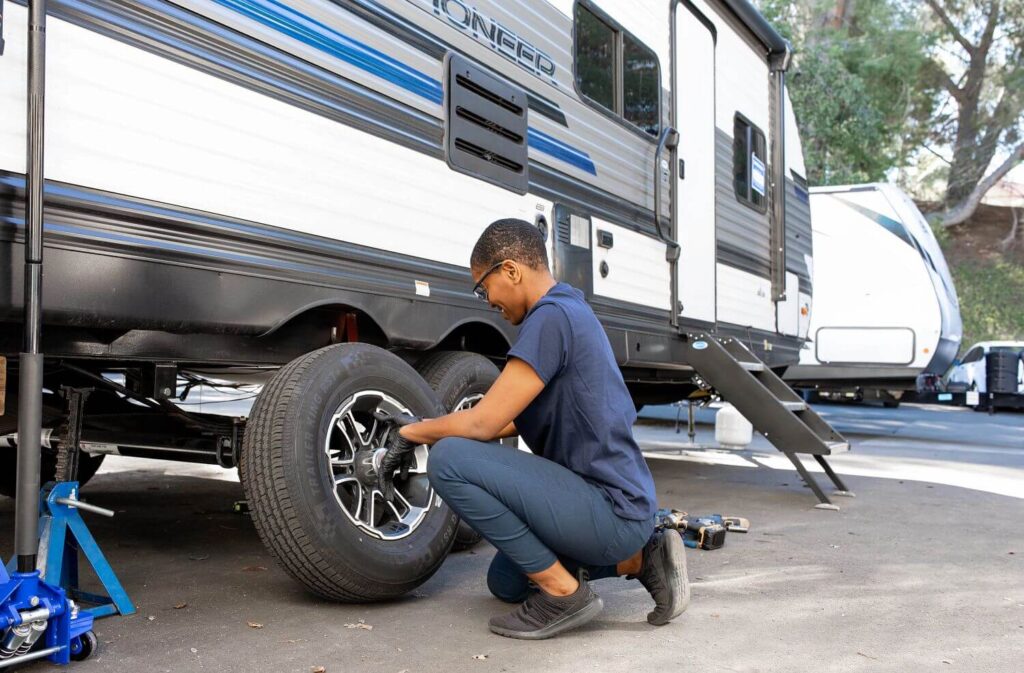 Female RV technician changing tire on dual axle travel trailer