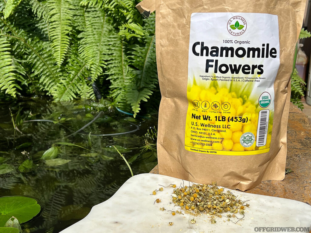 A bag of chamomile flowers with some of the flowers displayed on a bench.