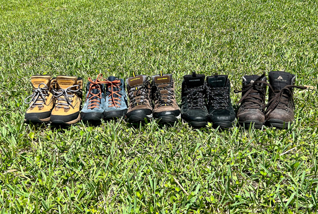Photo of a five pairs of boots lined up in a row in the grass.