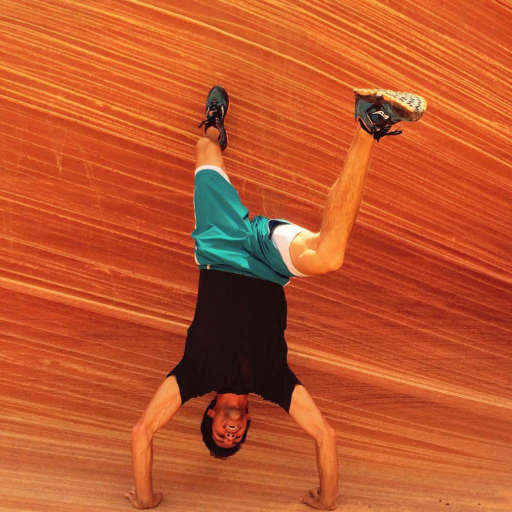 Man doing a handstand in front of red sandstone rock formation at the Wave in Arizona