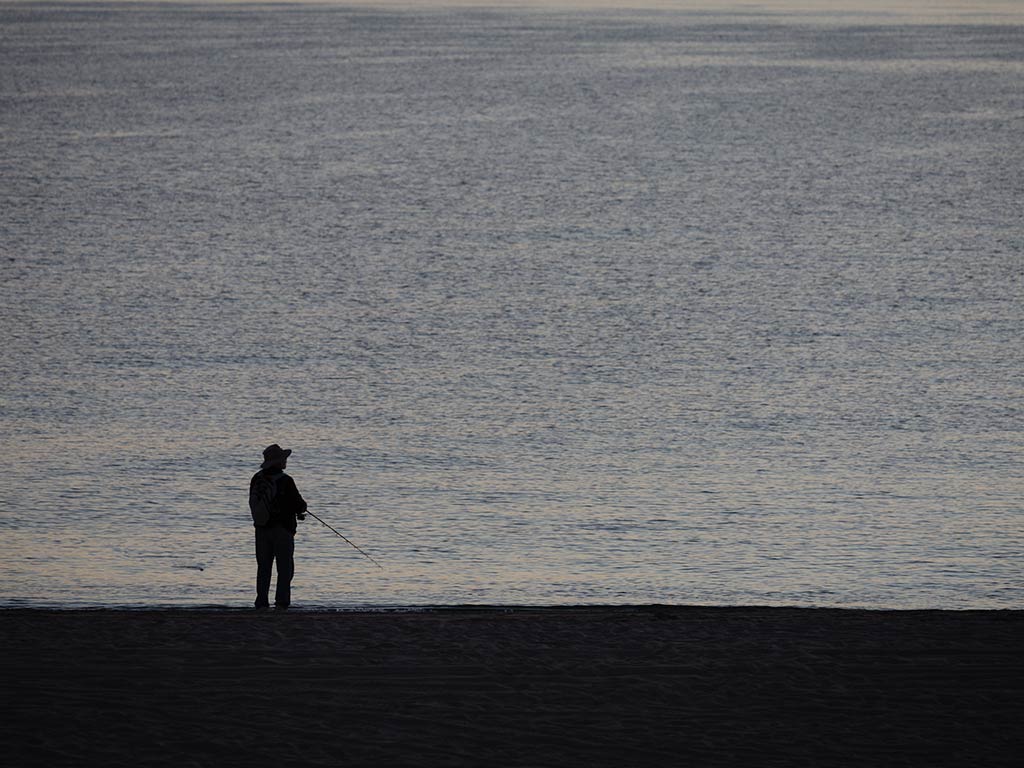 A view from behind of a lone angler fishing from the beach in Baja California Sur at sunset