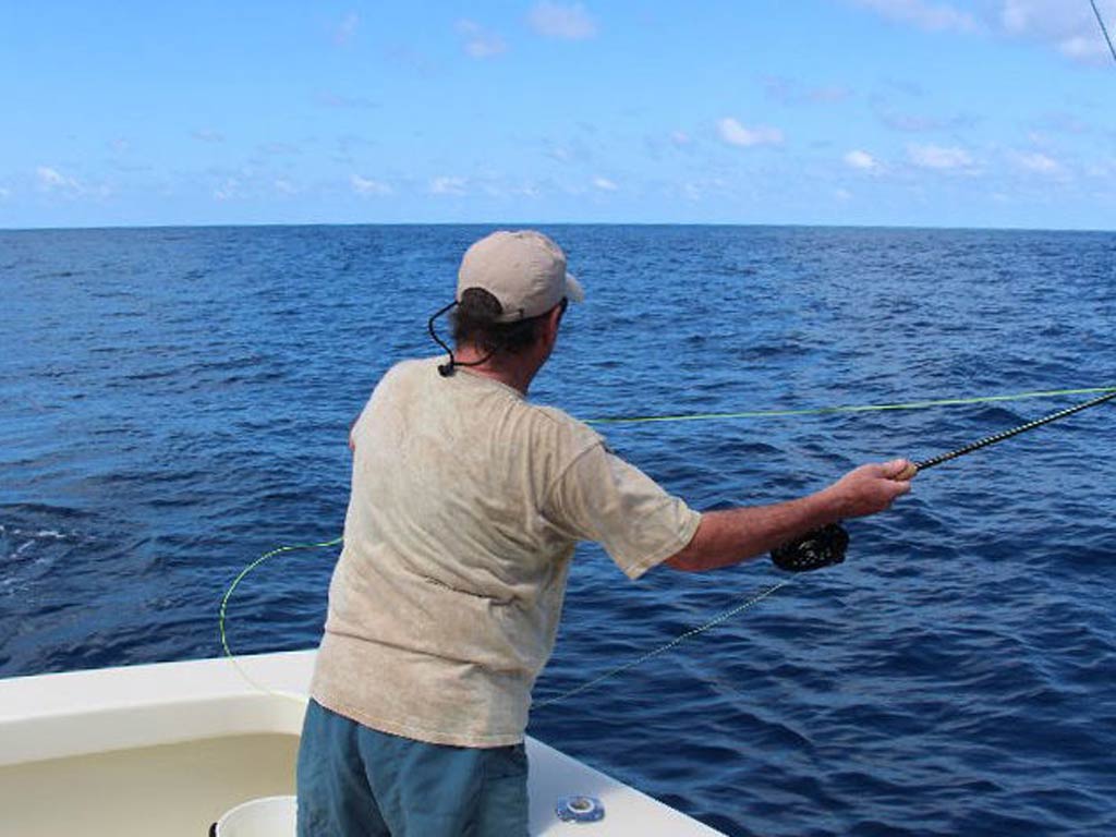 A back view of an angler casting the line while fly fishing offshore from a charter boat