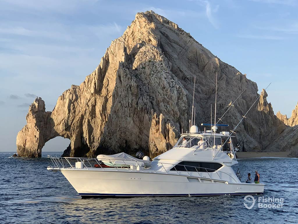 A view of a large offshore sportfishing boat in front of the famous Los Arcos near Cabo San Lucas, with the arch visible to the left of the image