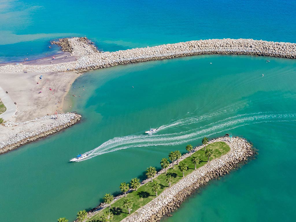 An aerial view of two sportfishing boats making their way back into the harbor between two jetty walls in San Jose Del Cabo on a clear day