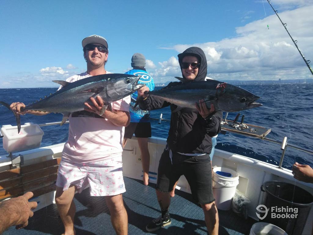 Two male anglers, smiling and holding a Tuna each on an offshore sportfishing vessel from Moreton Bay on a sunny day