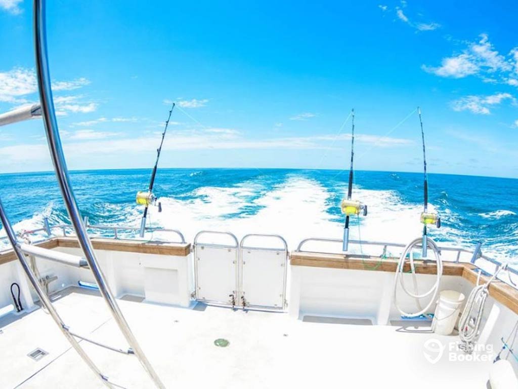 A view across the deck of a deep sea fishing boat in Perth on a clear day with three trolling rods set up, trolling beyond the wake of the boat