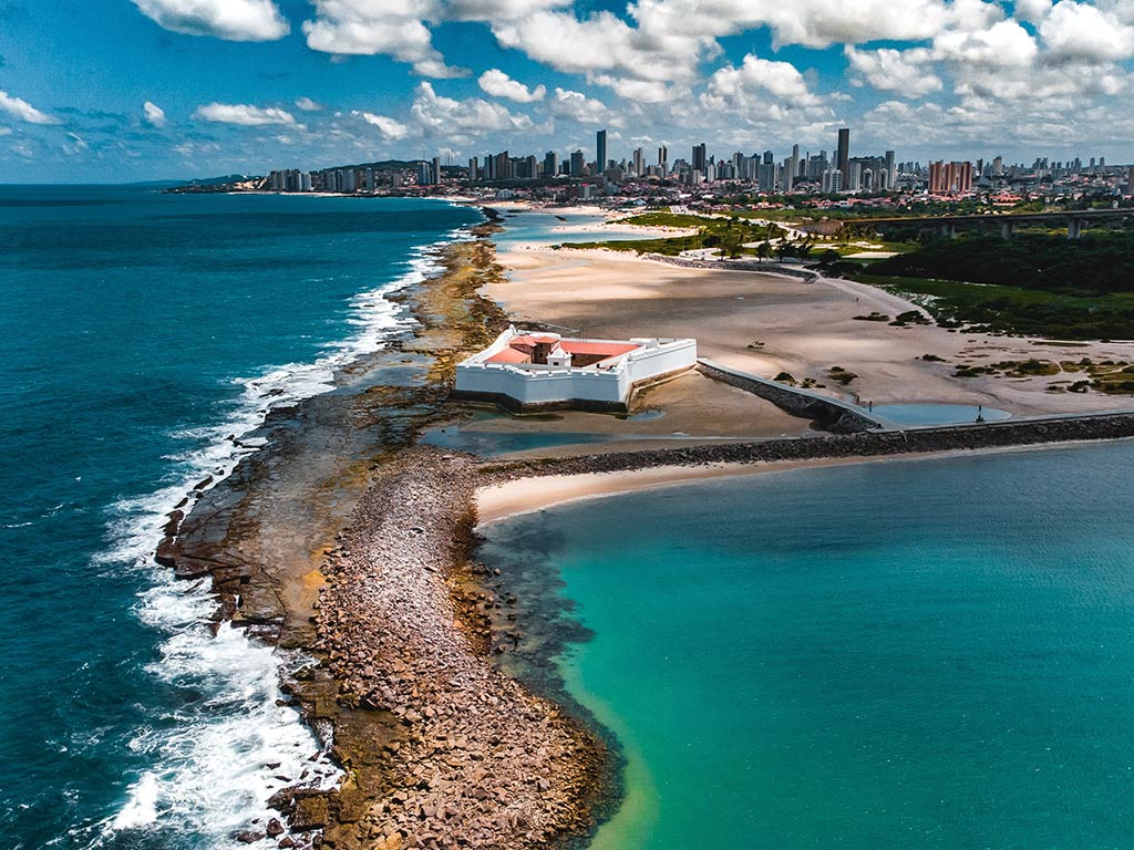 An aerial view of a spit of sand near Natal, Brazil, separating the Atlantic Ocean from the inshore lagoons, with the city visible in the distance on a bright day