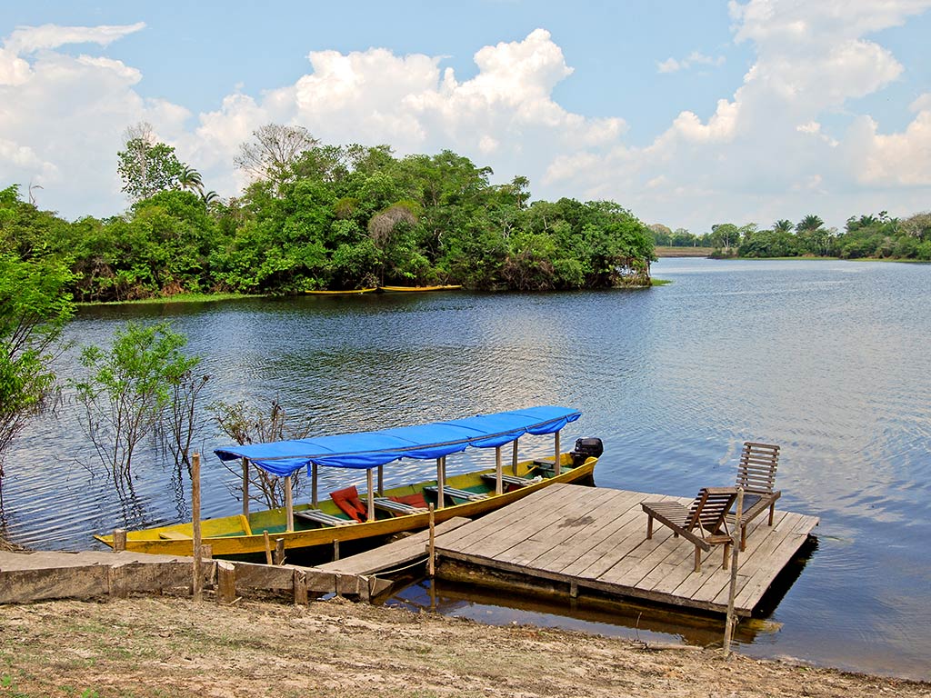 A view looking towards the Amazon River with a small fishing boat visible next to a small dock and two deckchairs laid out, with a green bank visible in the distance