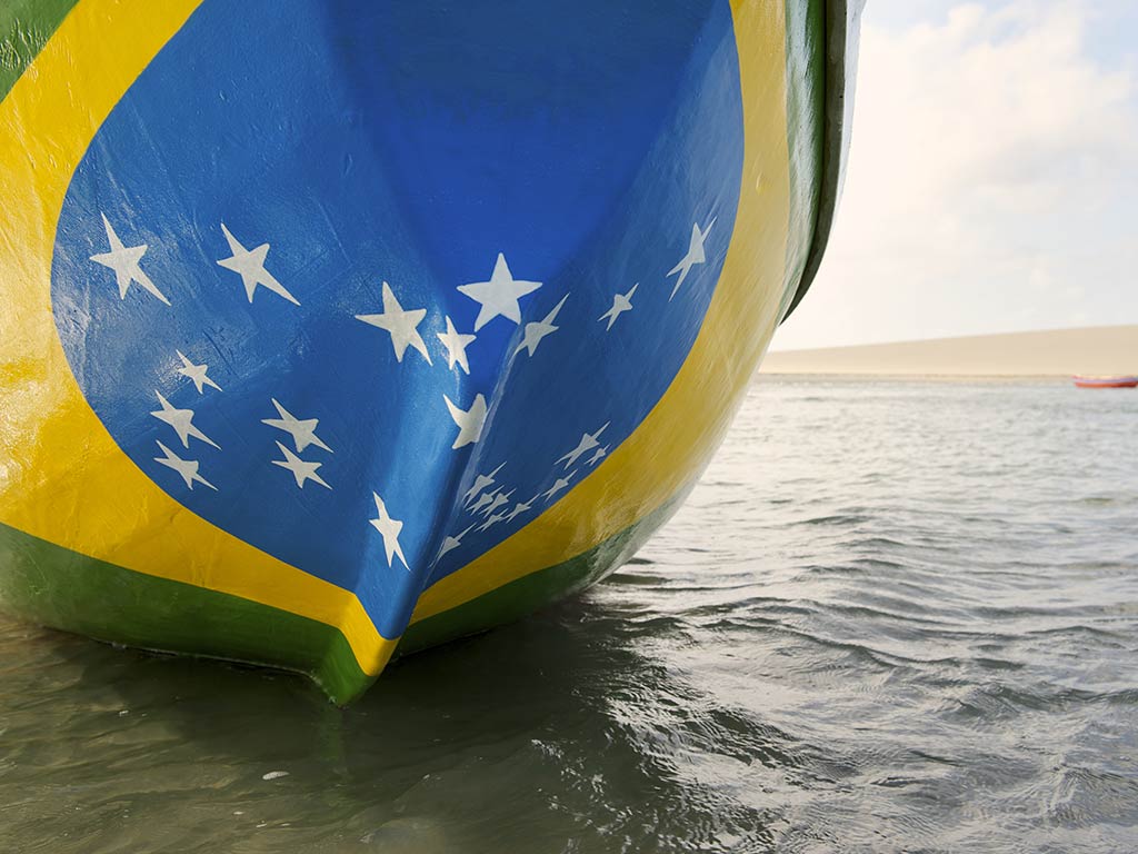 A closeup view of the bottom of a fishing boat painted in the colors of the Brazil flag in shallow waters on a day with sunny intervals