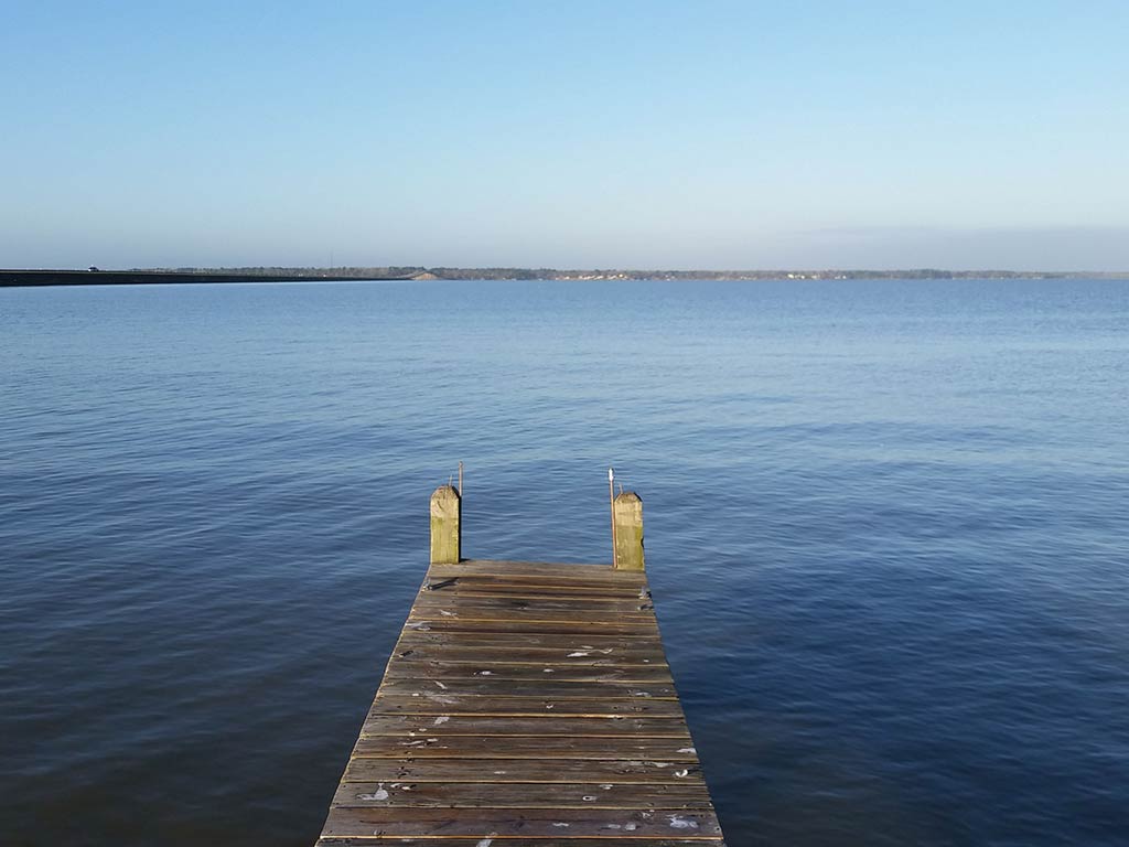 A view out to the calm waters of Lake Livingston on a clear day across a small wooden dock, which could be used for boats or fishing