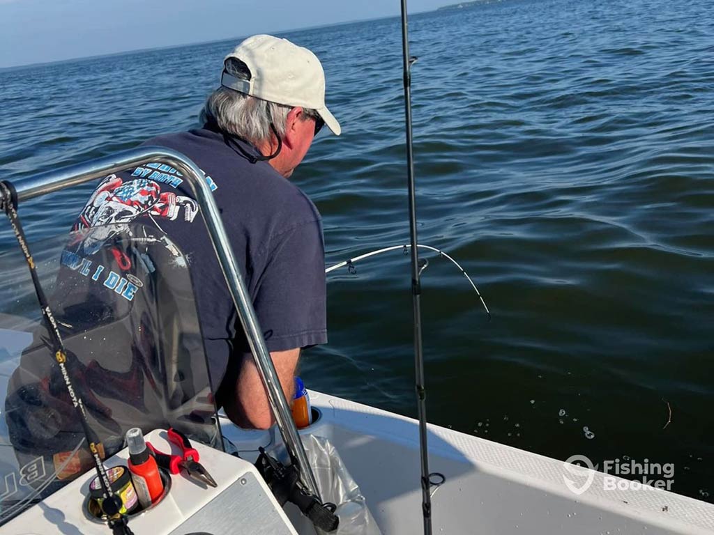 A view from behind of a grey-haired angler in a baseball cap and t-shirt fishing into the pristine waters of the south end of Lake Livingstone near its namesake city on a sunny day