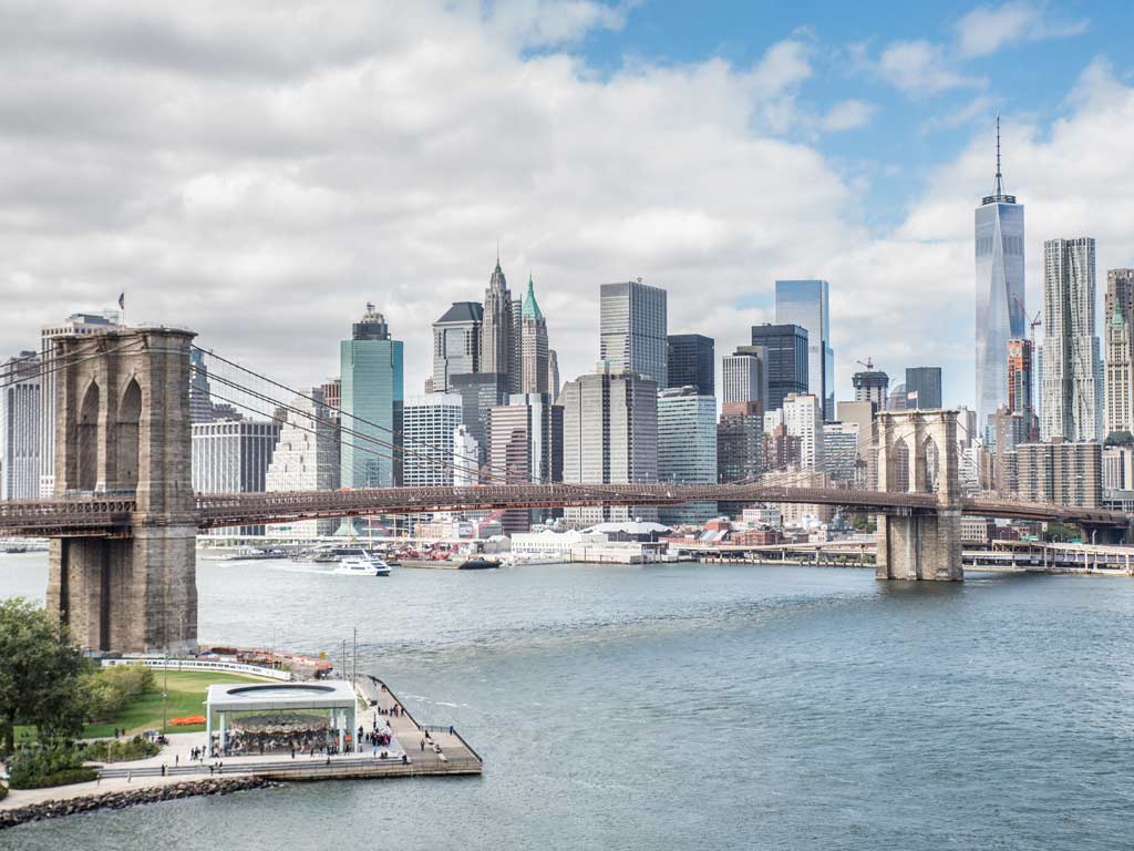 A view of the New York City skyline on a cloudy day taken from the East River, the Brooklyn Bridge is partially covering the skyscrapers visible in the background.