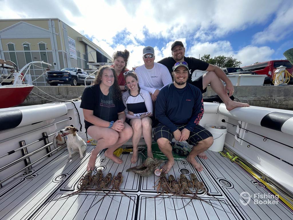 A family of six sitting on a fishing charter behind their catch of Lobster while back at the dock on a clear day