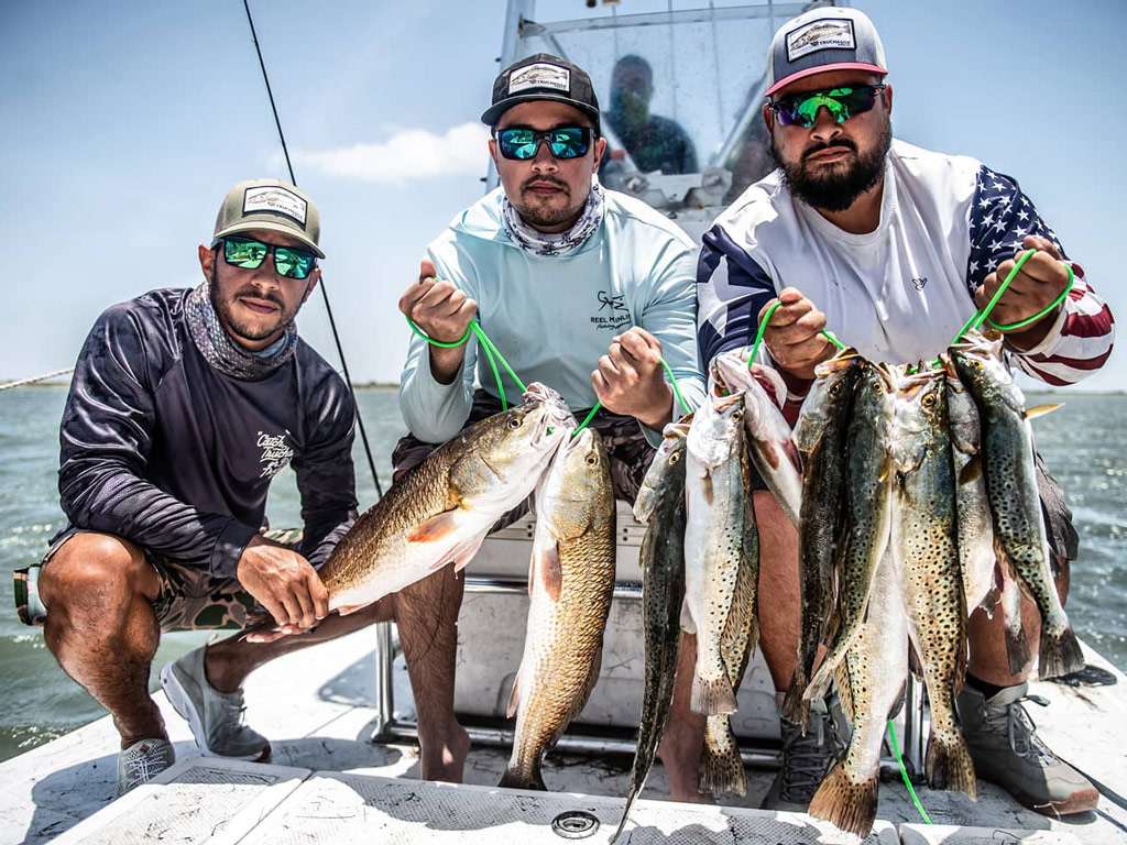 A photo of three anglers posing on a charter boat in South Padre Island in Texas holding Redfish and Speckled Trout caught during a winter fishing trip