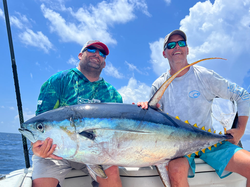 A photo of two proud anglers sitting on a charter fishing boat and posing with a huge Yellowfin Tuna they caught while deep sea fishing out of Biloxi in Mississippi