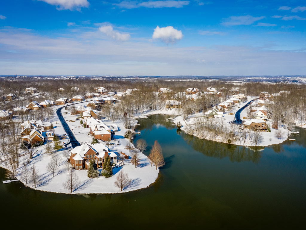 An aerial view of the lake and snow-covered settlement depicting idylic houses and trees in Central Kentucky during winter