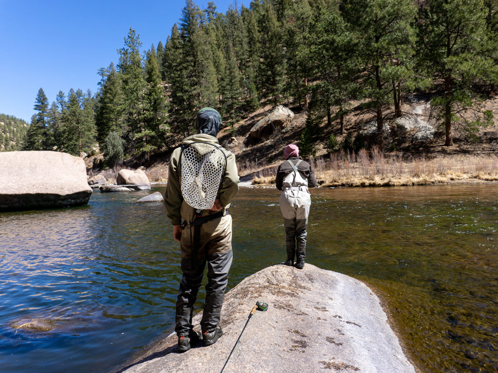 A photo of two fly fishing anglers standing on a big rock getting ready to fly fish on the South Platte River in the Cheesman Canyon area near Denver in Colorado during late fall and early winter