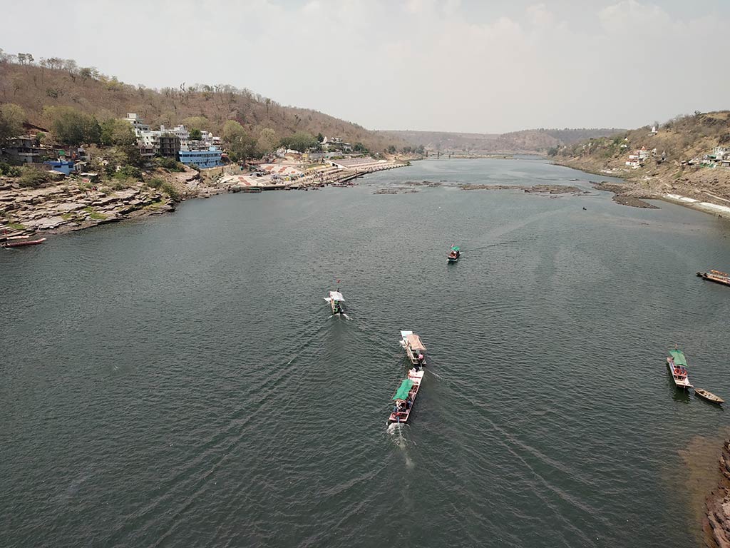 An aerial view of a tributary river to the Narmada River in India on a cloudy day, with a number of fishing boats visible in the wide river