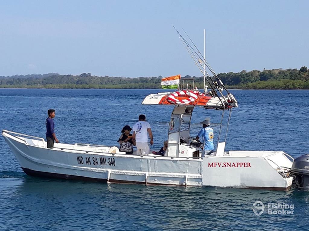 A view across the water towards a long fishing boat in the inshore waters of India on a clear day, with an Indian flag visible above the console and a group of people milling about