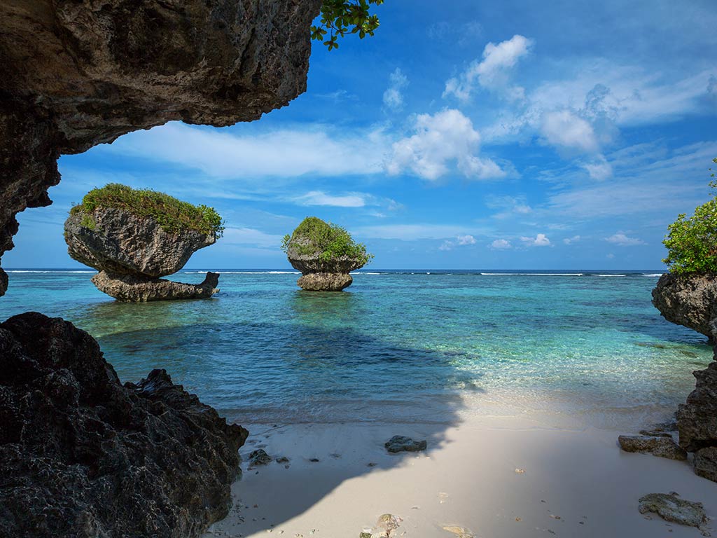 A view from a beach in Guam towards some interesting rock formations in the sea on a clear day