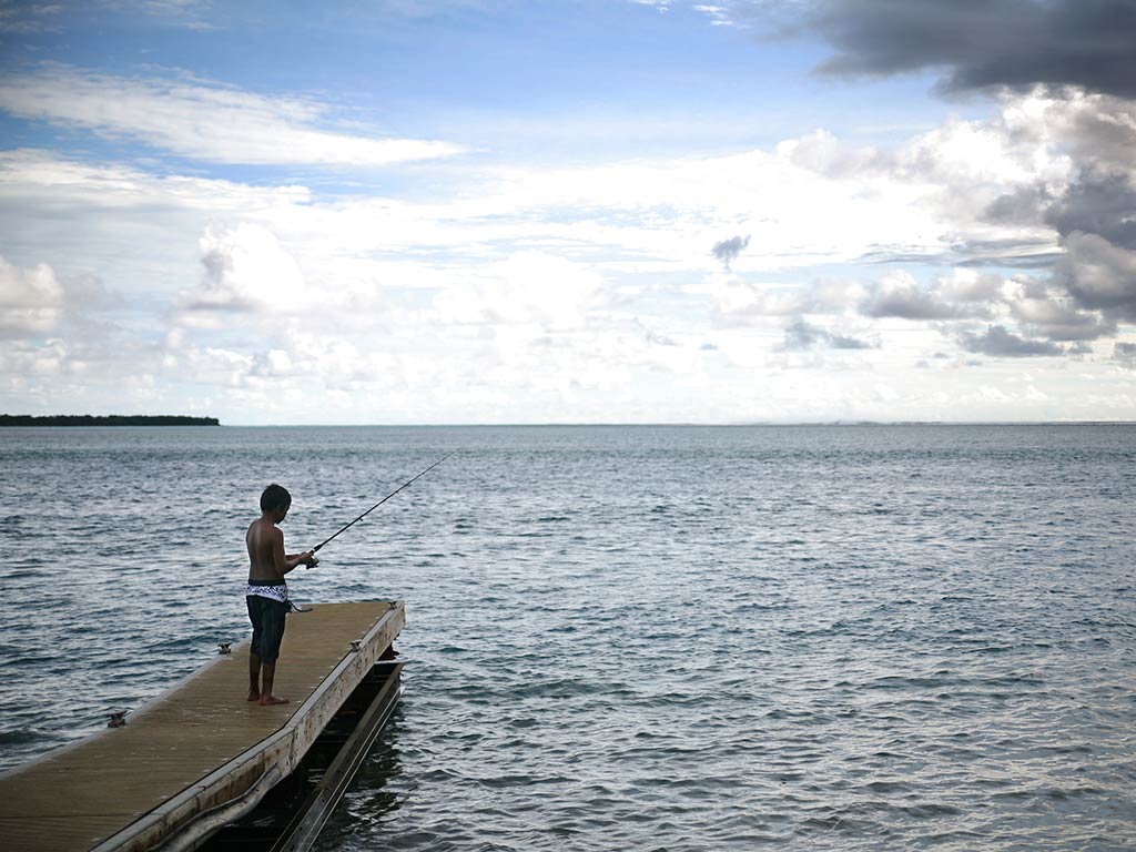 A view towards the ocean from North Mariana Island in Guam, where a lone angler is fishing from a small pier on a cloudy day