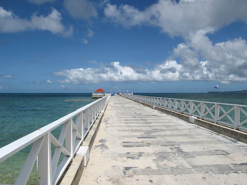 A view along a fishing pier on Coco's Island, Guam, on a clear day, with crystal clear waters visible either side