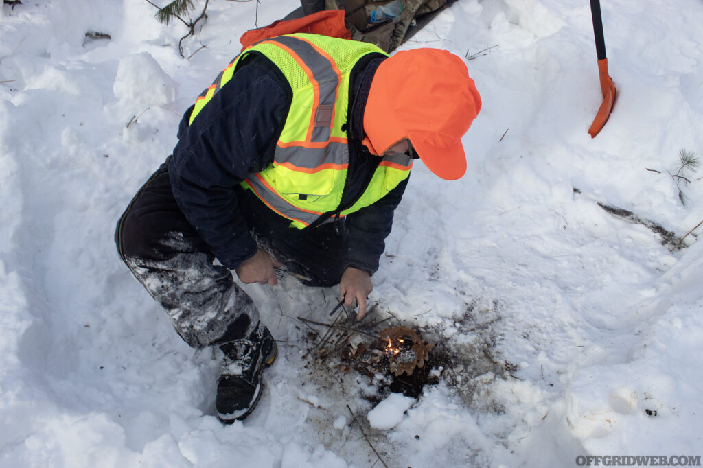 Photo of a man starting a small survival fire in the snow during winter survival training.