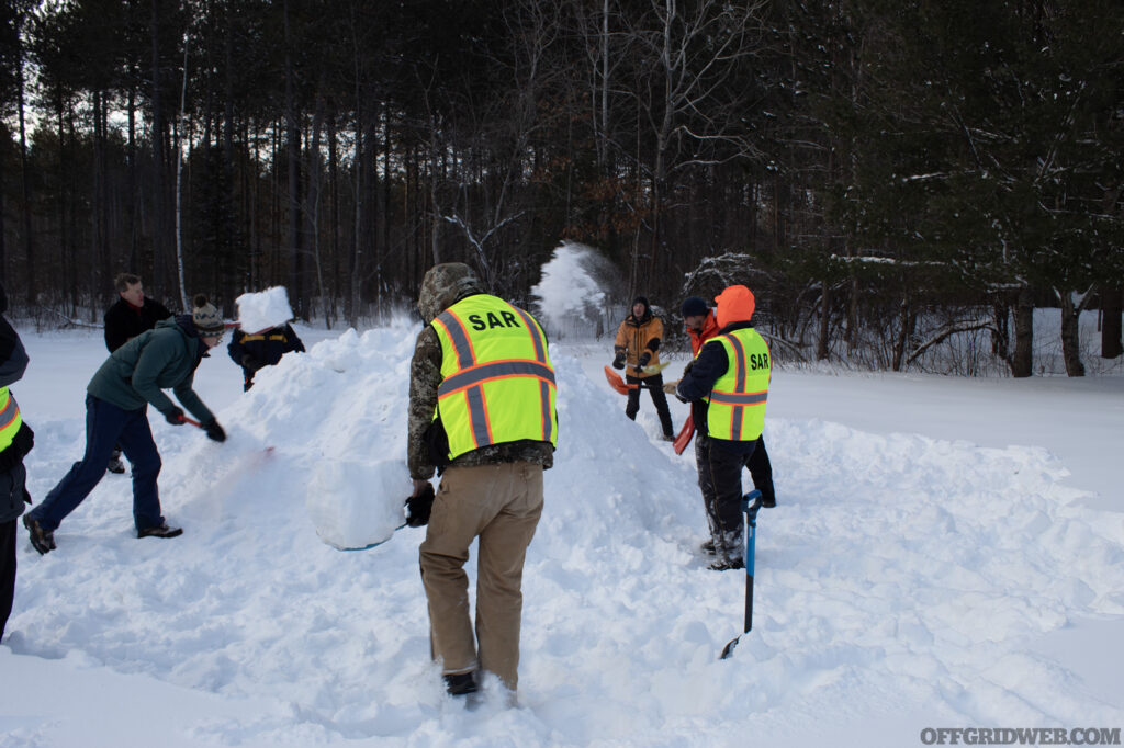 Photo of winter survival students piling snow into a large mound as the first step of building a quinzee hut.