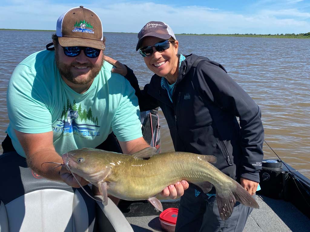 Two anglers on a boat, posing for a photo with a sizeable Channel Catfish they caught