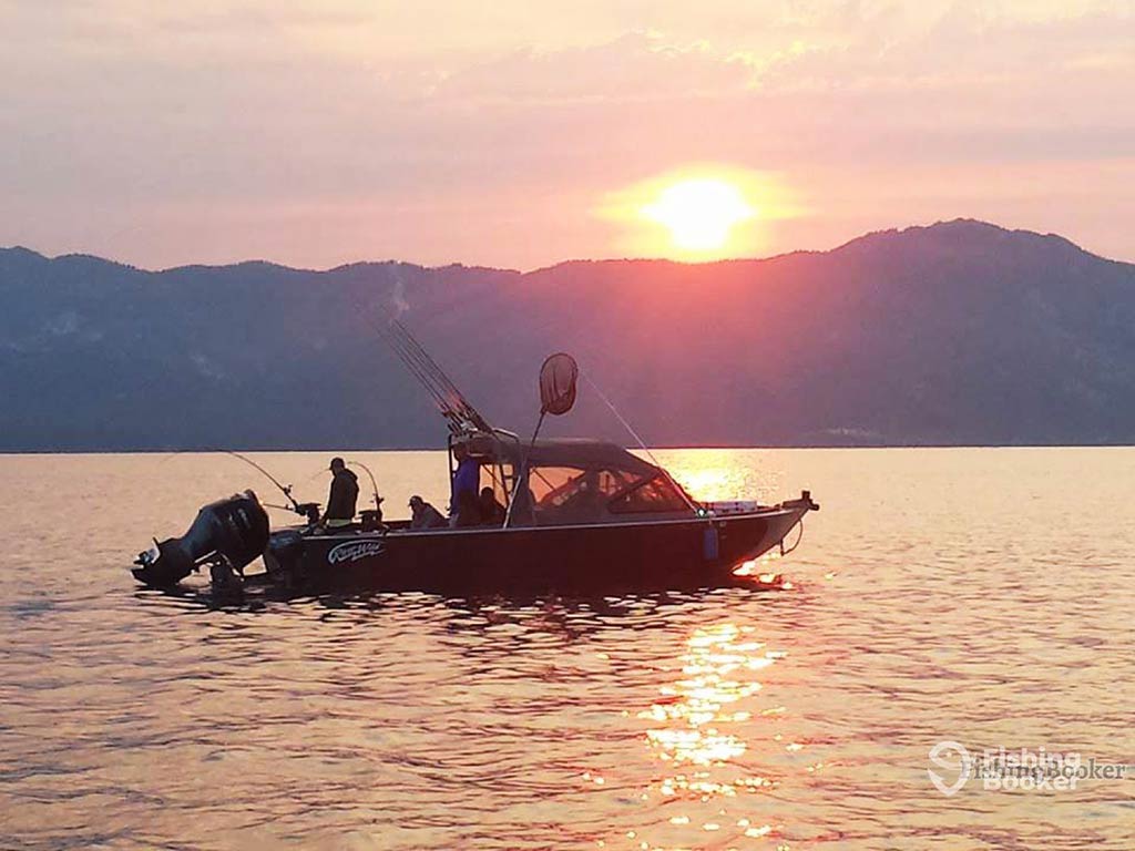 A view across the water towards a fishing charter on a lake in Nevada at sunset on a clear day, with the sun setting in the distance behind a mountain