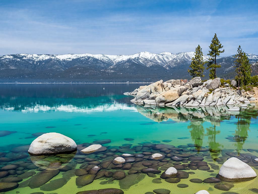 A view from a rocky shoreline in eastern Lake Tahoe of the crystal clear waters and snow-capped mountains in the distance