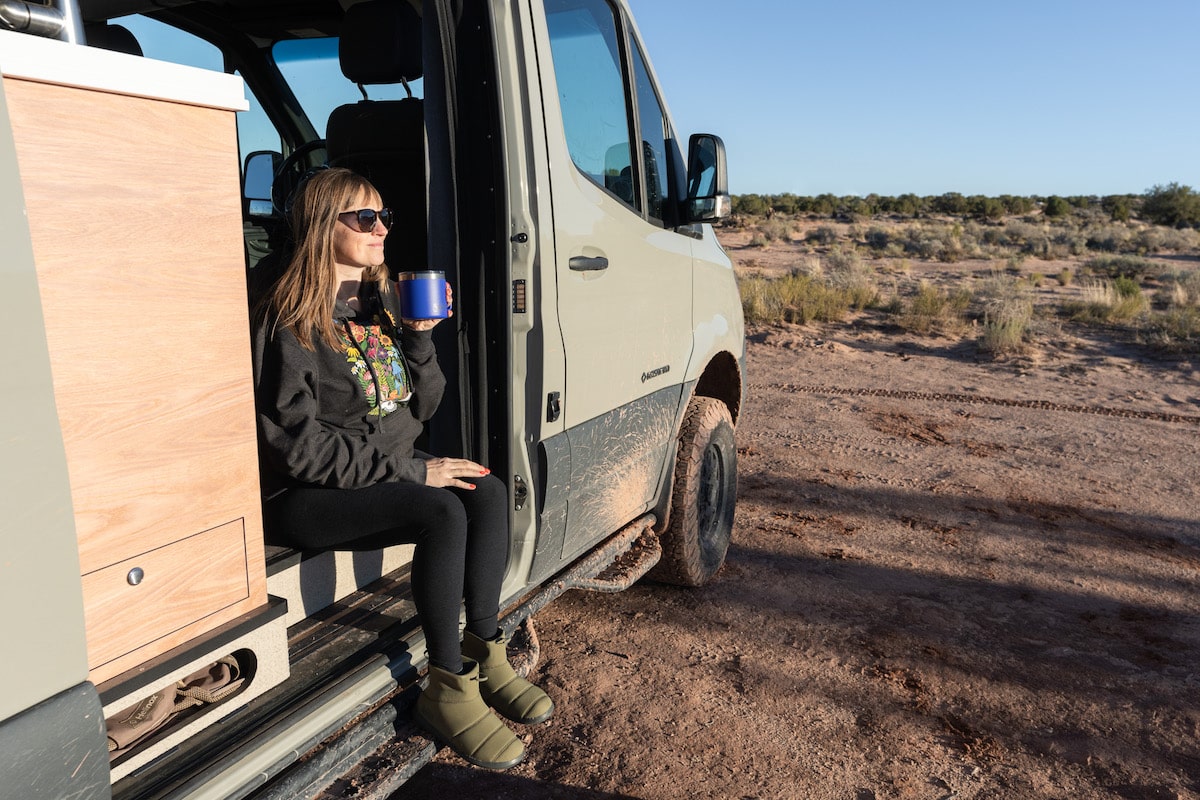 Bearfoot Theory founder Kristen Bor sitting on edge of Sprinter Van drinking coffee in Moab.