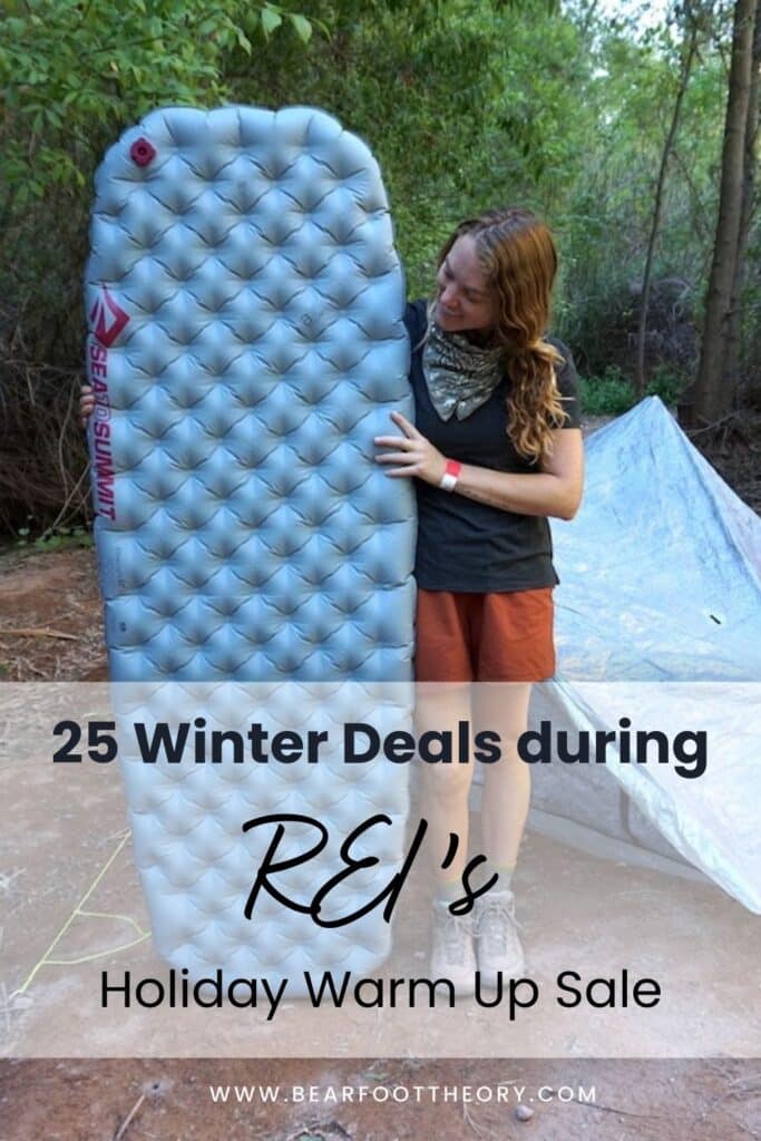 Pinterest image with text that reads "25 winter deals during REI's holiday warm up sale." Image shows a woman holiday an inflated sleeping pad in front of her tent at a campsite.
