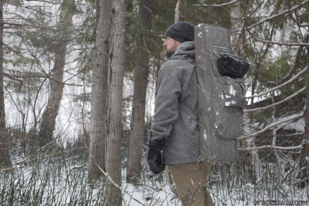 Photo of a man walking through a winter forest with a firearms case being worn as a backpack.