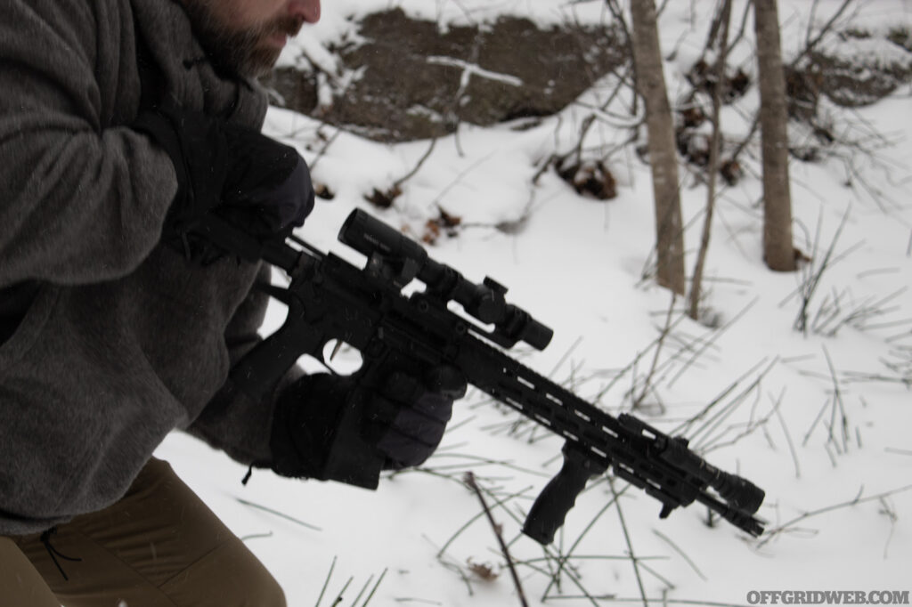 Photo of a man pulling the charging handle of a winter ready AR to the rear.