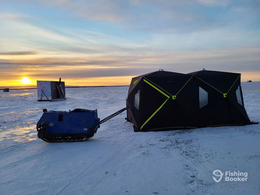 A view across a frozen lake at sunset towards a couple of temprary ice huts used for ice fishing in Ontario on a bright day