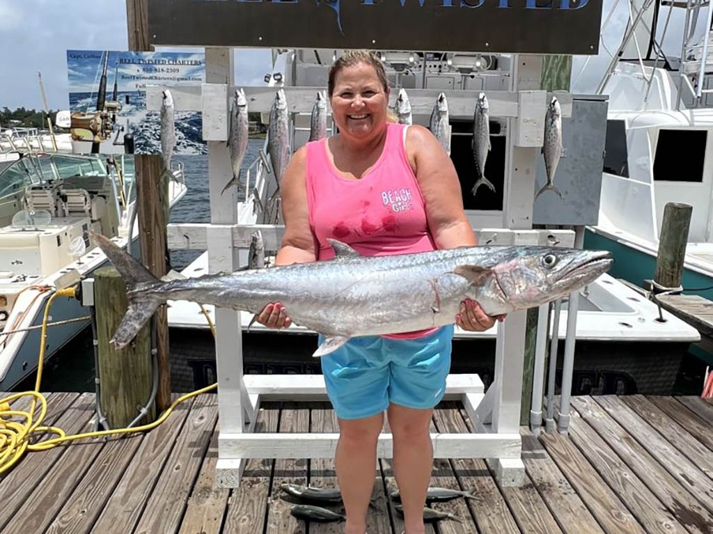 A woman in a pink vest shirt standing on a dock after a fishing trip in Panama City while holding a large Kingfish with a number of other small fish behind her