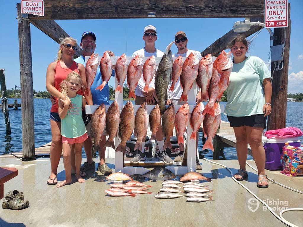 A family of anglers of different ages and genders posing with their haul of different Snappers and a Gag Grouper after a successful fishing trip in Panama Beach on a sunny day