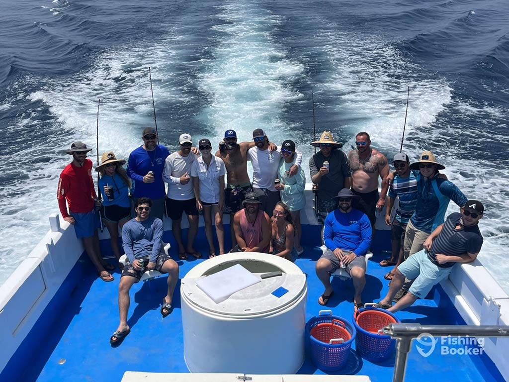 A view from the flybridge of a party fishing boat in Panama City, FL, looking down towards a large group of anglers gathered on the deck and posing for a photo with the wake of the boat visible behind them