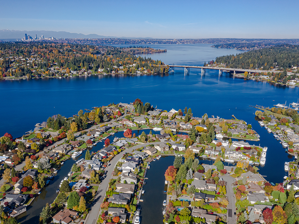 An aeial autumnal view of Lake Washington from Newport Shores with a residential neighbourhood with canals and boats in the foreground and Seattle and the floating bridge in the background