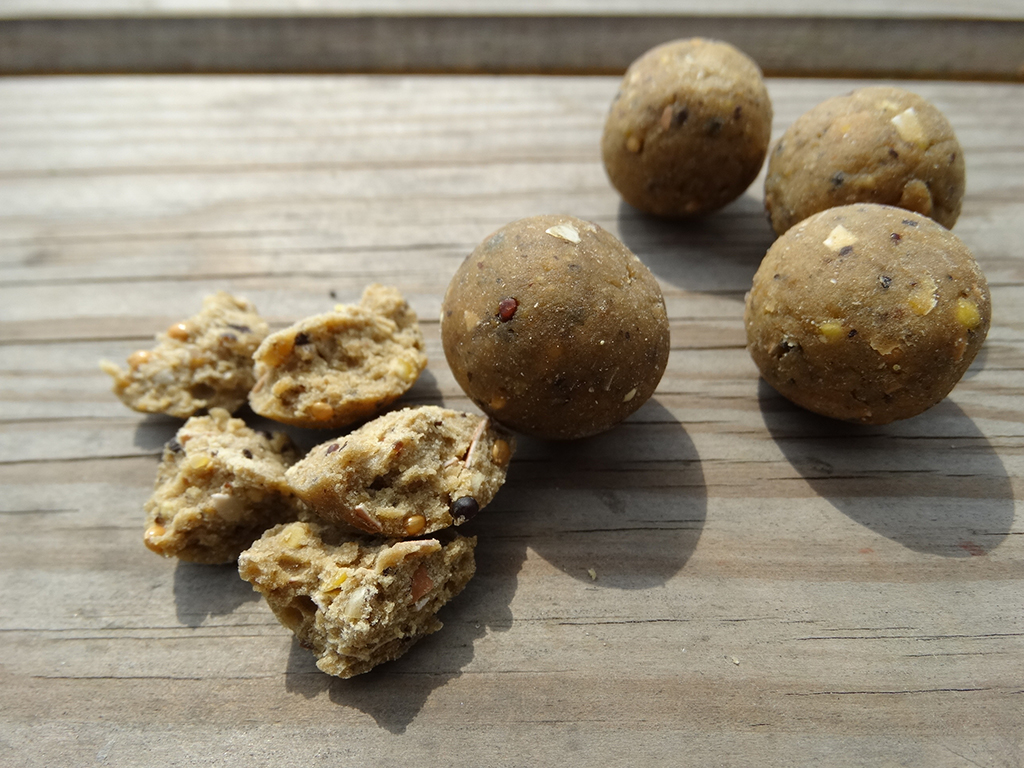 Four whole balls of bait and one ball broken apart to show the contents against a wooden background