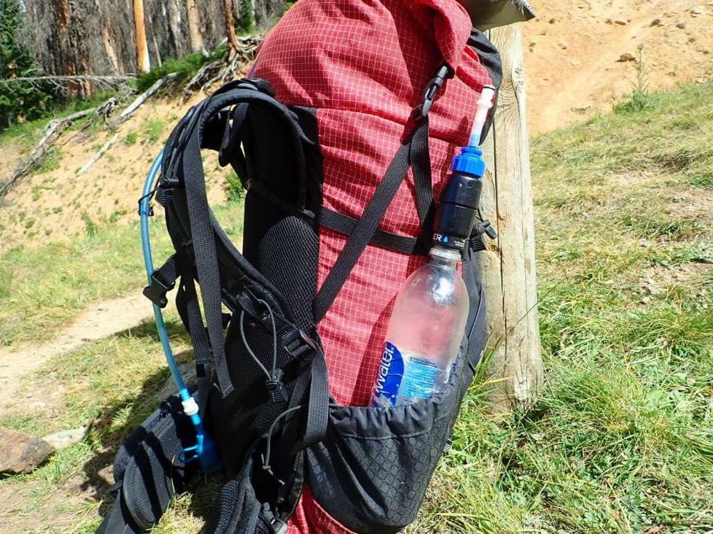 Smartwater bottle with Sawyer filter in side pocket of red ULA Circuit backpack leaning against post