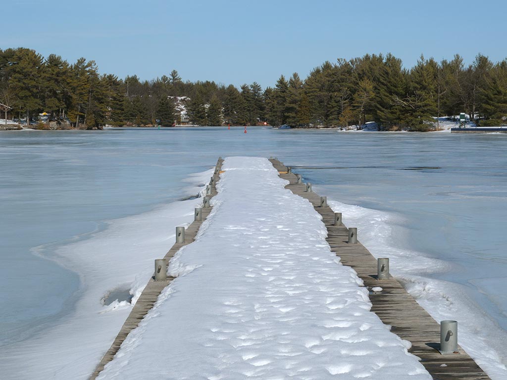 A pier covered in snow overlooking a frozen lake in the Muskoka district, Canada, with trees in the distance