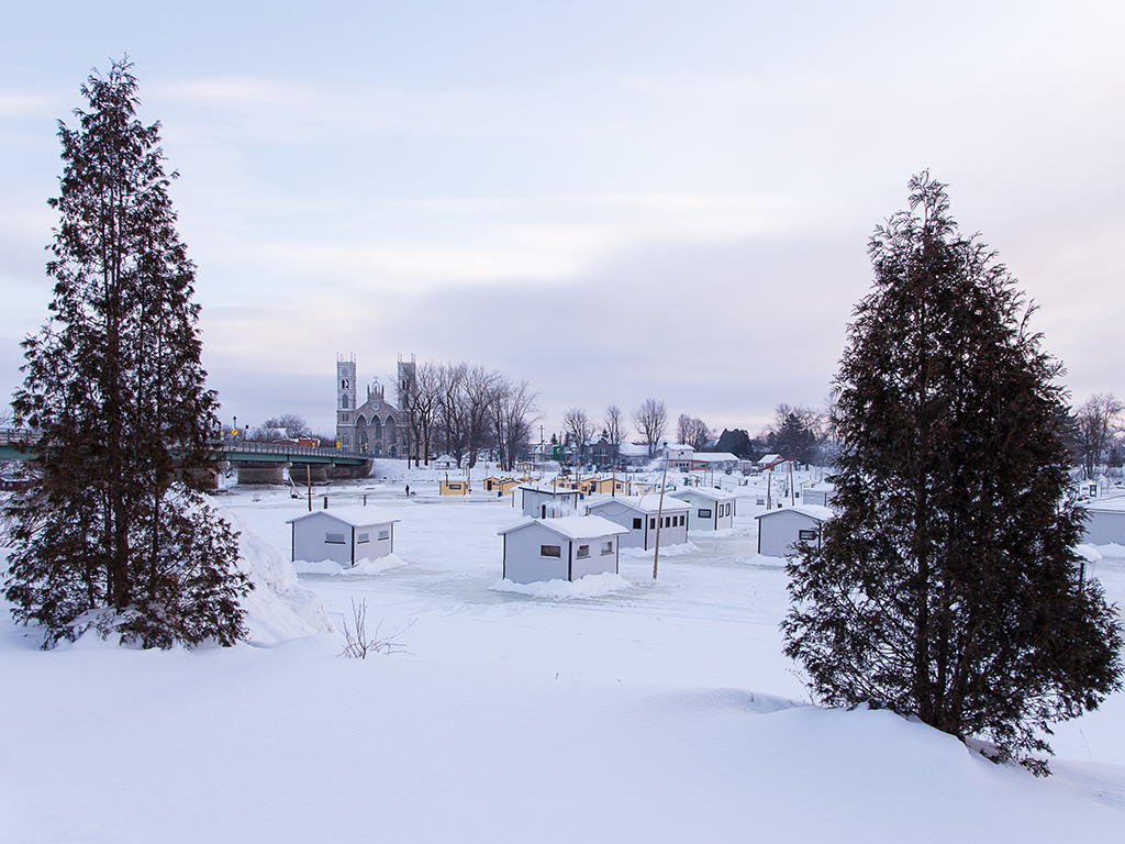 A view of a "village" of ice fishing cabins occupies the Sainte-Anne River in Sainte-Anne-de-la-Pérade, Quebec. A church and a bridge across the frozen river are visible in the background