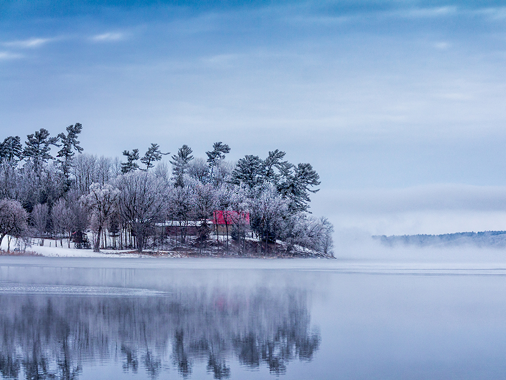 An island on Muskrat Lake in Canada is reflected on the cold water in the winter